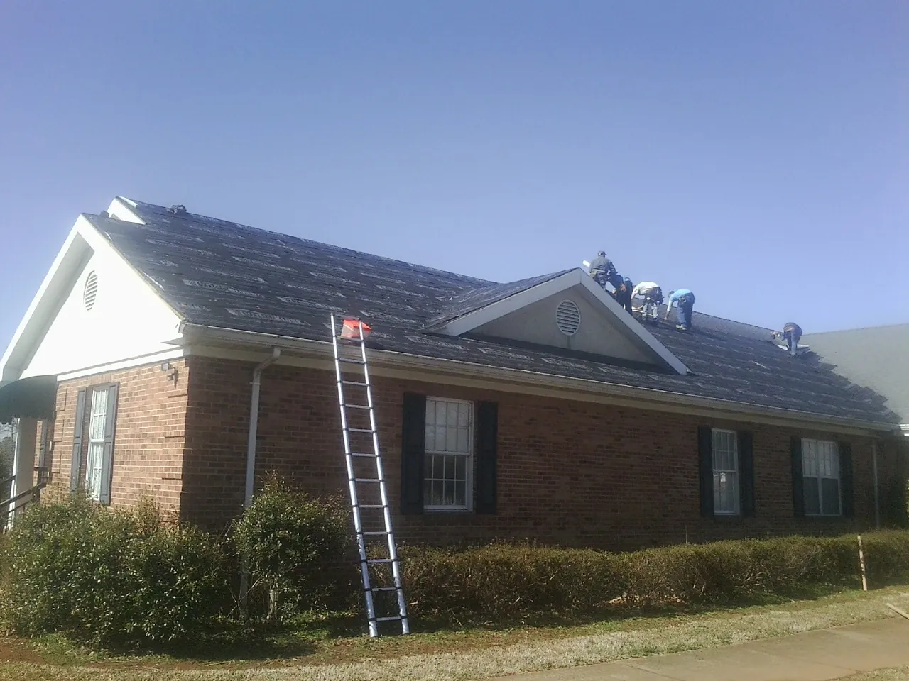 Crew tearing shingles off a brick ranch roof with a ladder set — Emergency Roof Repair work by our crew in Nuremberg