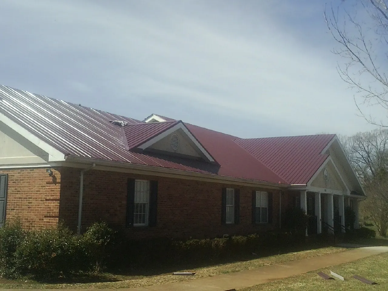 Red metal roof with gabled entries on a long brick building, from a Hail Damage Roof Repair job in Nuremberg