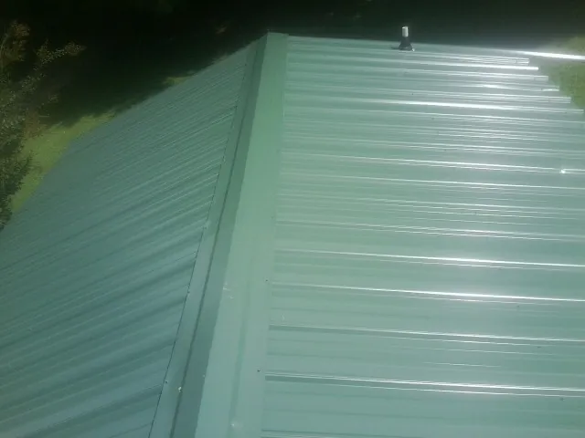 New green metal panels meeting at the ridge of a roof — Flat Roof Repair work by our crew in Nuremberg