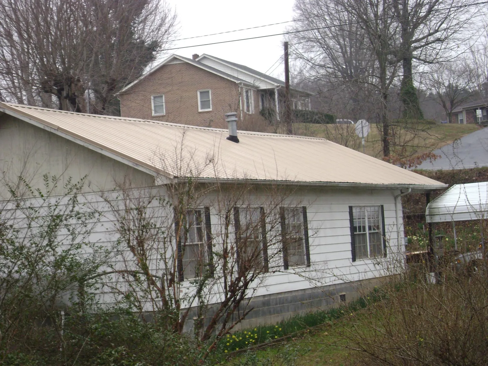 Tan metal roof on a white sided house set into a hillside — Commercial Roofing by Roofing Brothers in Nuremberg